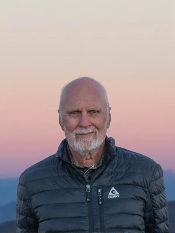 Richard Ambrose outdoors at dusk with mountains in the background.