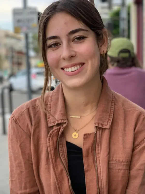 Clare Schumann seated outdoors at a sidewalk table on a city street.