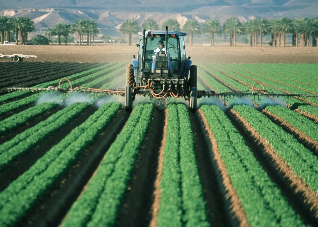 tractor spraying pesticides on rows of crops