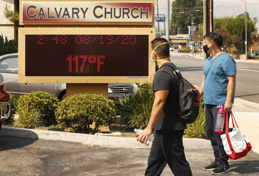 Two people in front of the Calvary Church display board in Woodland Hills. The board displays a temperature of 117 degrees Fahrenheit on August 19, 2020.