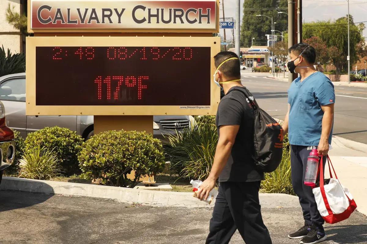 Two people in front of the Calvary Church display board in Woodland Hills. The board displays a temperature of 117 degrees Fahrenheit on August 19, 2020.