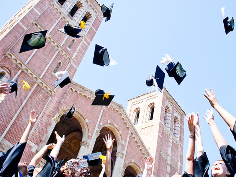 UCLA graduates toss their caps in the air in front of Royce Hall