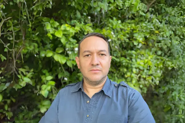 Felipe Zapata, co-director of the Center for Tropical Research, stands outdoors in front of dense green foliage.