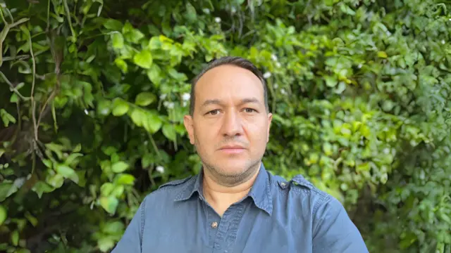 Felipe Zapata, co-director of the Center for Tropical Research, stands outdoors in front of dense green foliage.