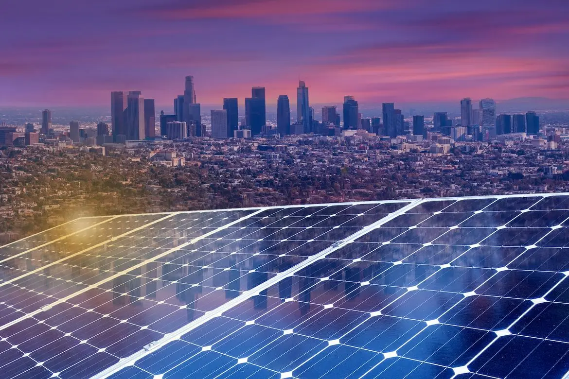 Solar panels in the foreground with the downtown Los Angeles skyline at sunset behind them.