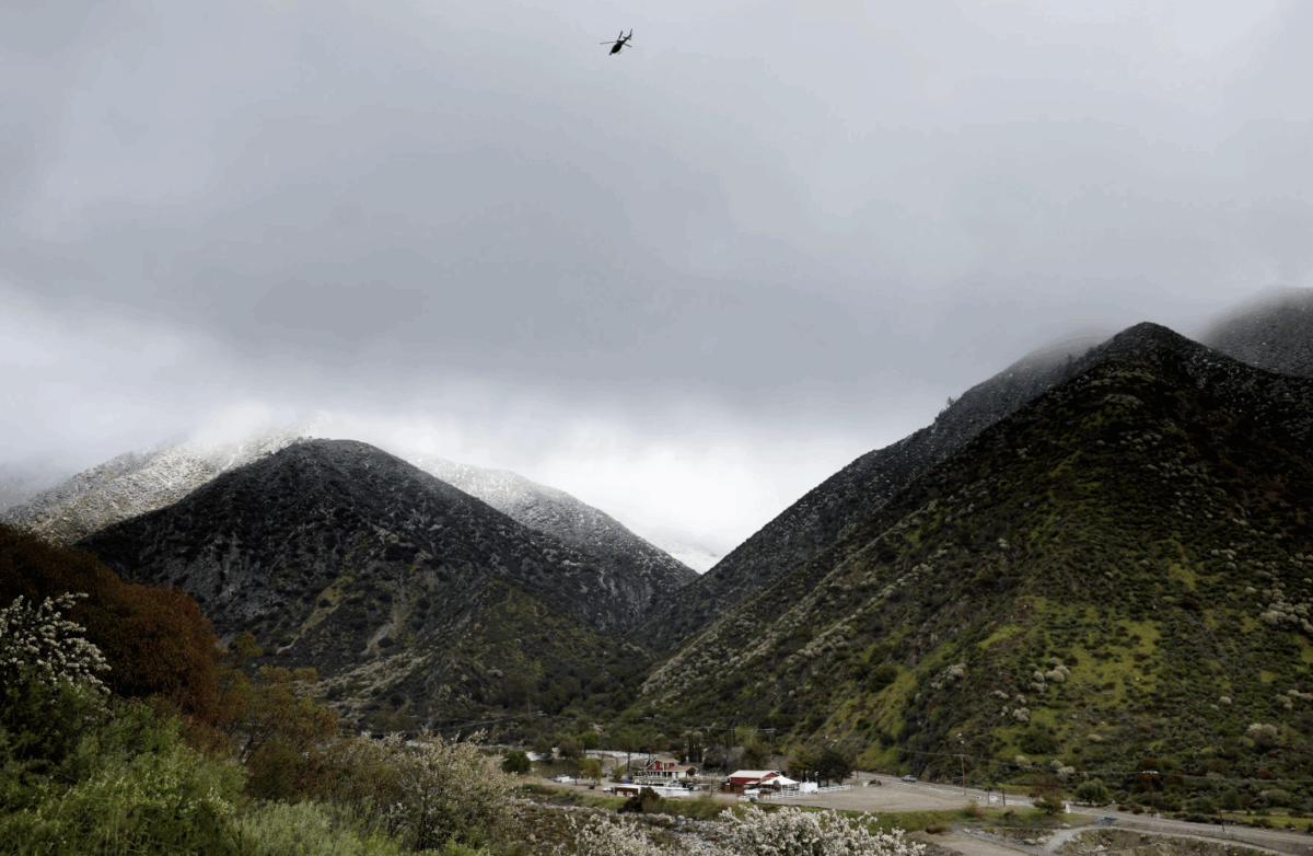 A helicopter flies above the foothills of the San Gabriel Mountains with a dusting of snow in the Angeles National Forest in Los Angeles County