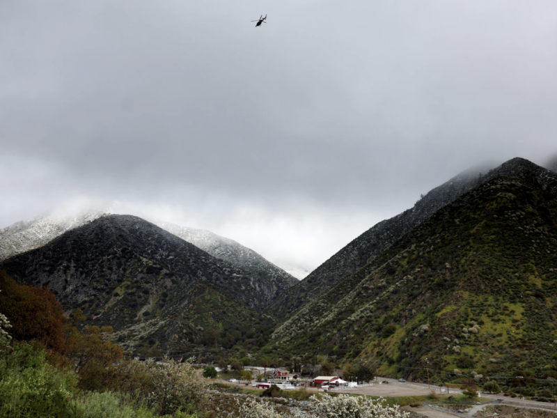 A helicopter flies above the foothills of the San Gabriel Mountains with a dusting of snow in the Angeles National Forest in Los Angeles County