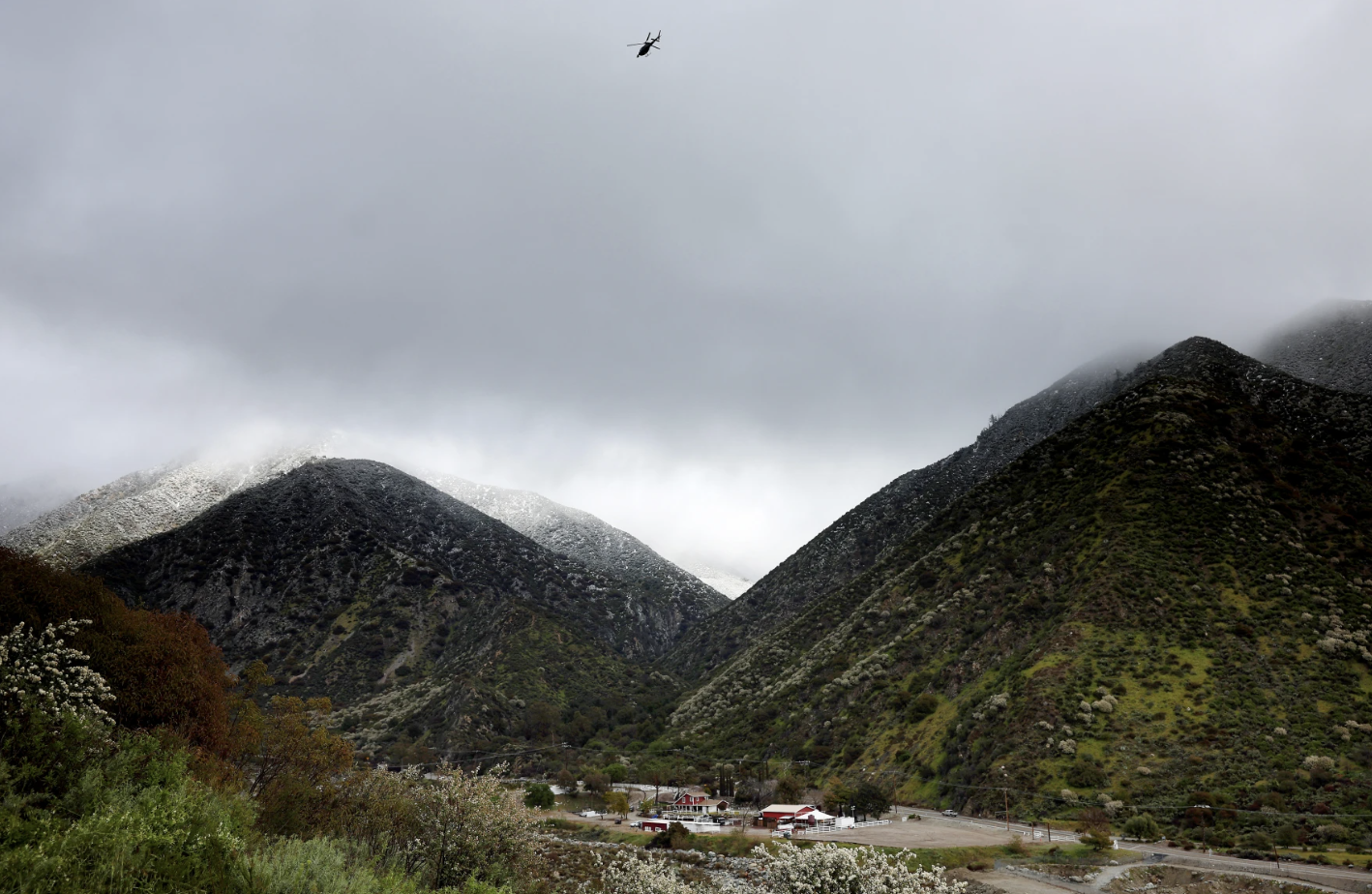 A helicopter flies above the foothills of the San Gabriel Mountains with a dusting of snow in the Angeles National Forest in Los Angeles County