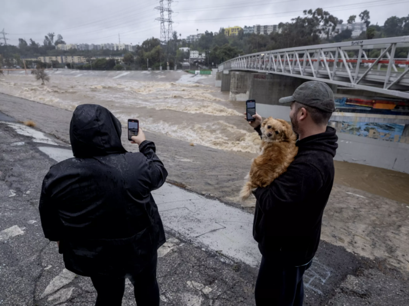 A couple take photos of a rain-swollen Los Angeles River near Atwater Village, in Los Angeles. (Ringo Chiu / For The Times)