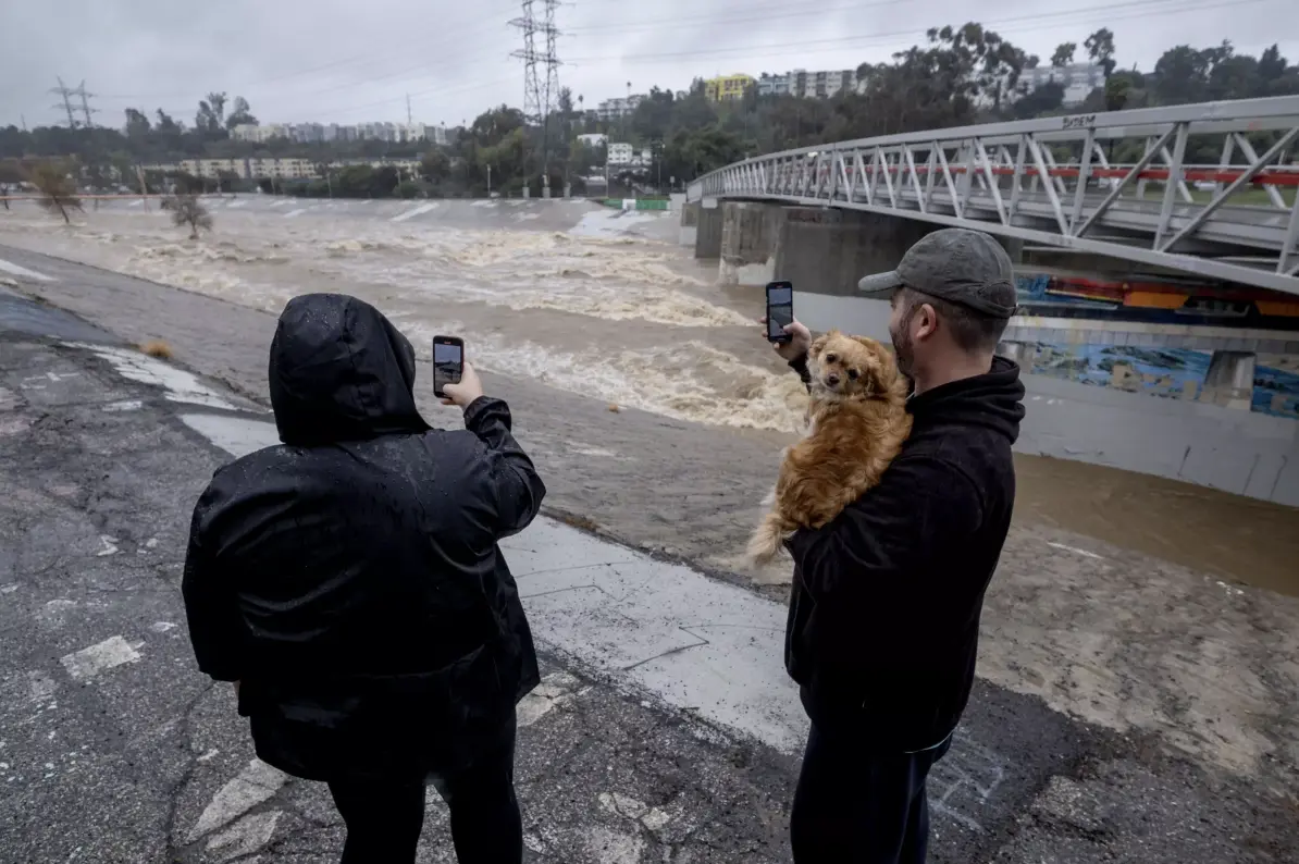 A couple take photos of a rain-swollen Los Angeles River near Atwater Village, in Los Angeles. (Ringo Chiu / For The Times)