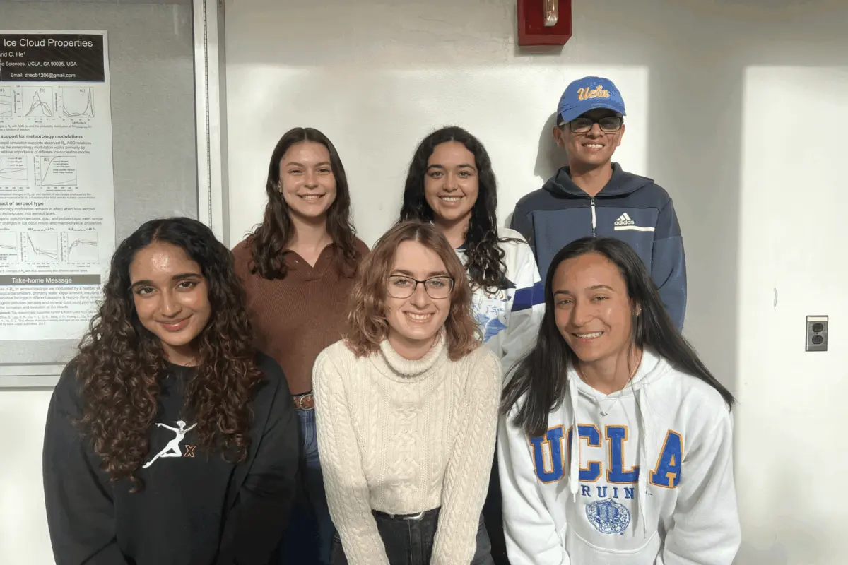 A group of six UCLA students posing together indoors beside a research poster on cloud properties.