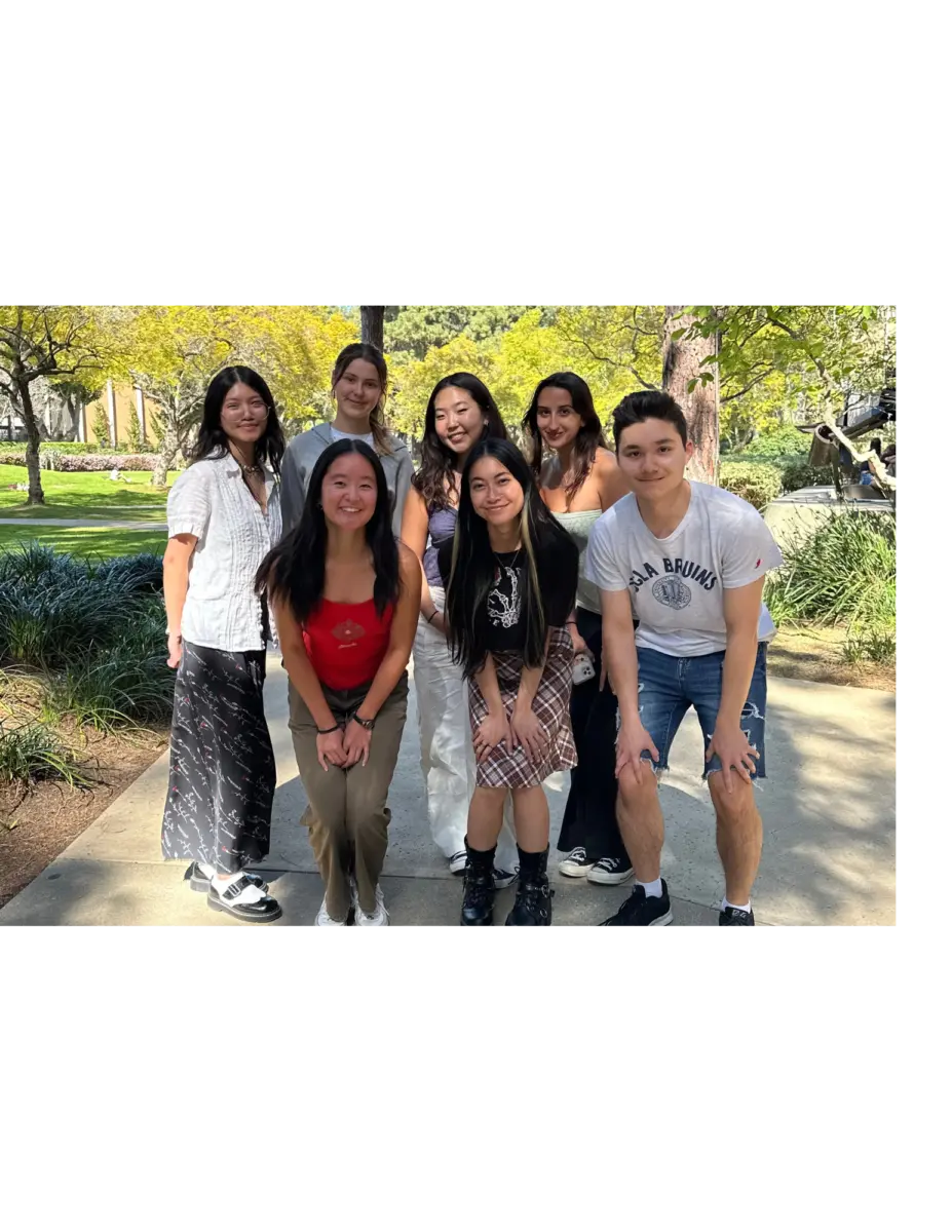 A group of seven students gathered together for a photo on a tree-lined campus walkway.
