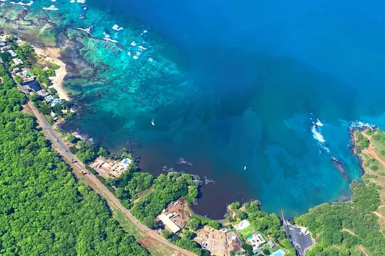 Aerial view of a Hawaiian coastline where a dark plume spreads through turquoise nearshore water below coastal homes and a road.