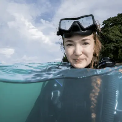 Callie Annette Veelenturf at the water's surface in dive gear, photographed half above and half below the waterline.