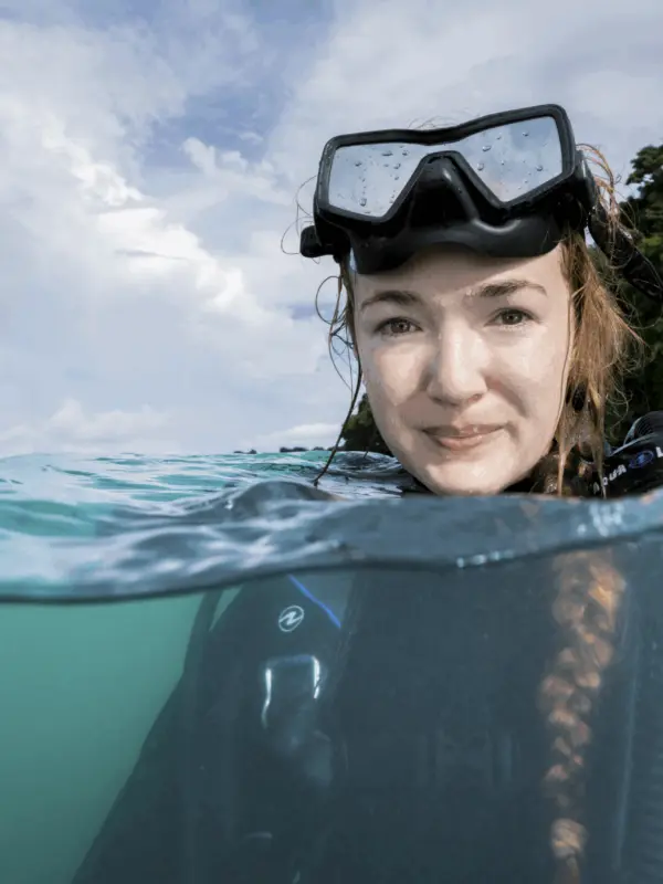 Callie Annette Veelenturf at the water's surface in dive gear, photographed half above and half below the waterline.