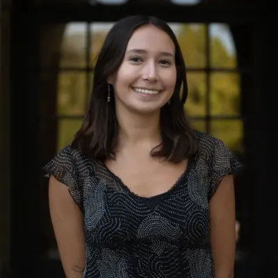 Maya Parra, standing outdoors in front of a paned window or door