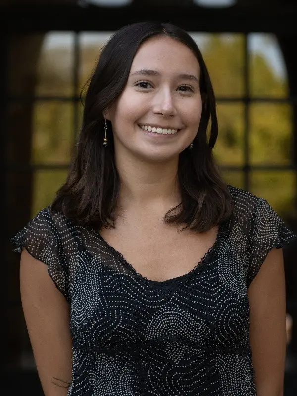 Maya Parra, standing outdoors in front of a paned window or door