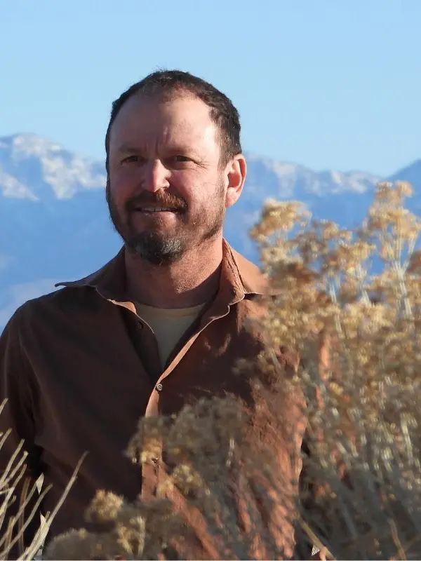 Dr. Dan Cooper standing among dry shrubs with snow-capped mountains behind him.