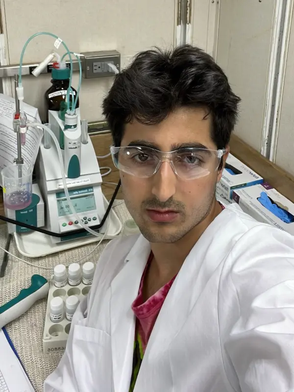 George Vetushko in a laboratory beside a titration setup and pipette rack.