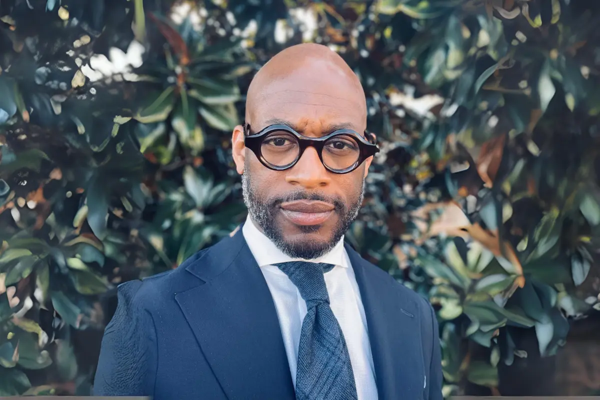 Dr. J. Kameron Carter stands outdoors in front of a leafy tree.