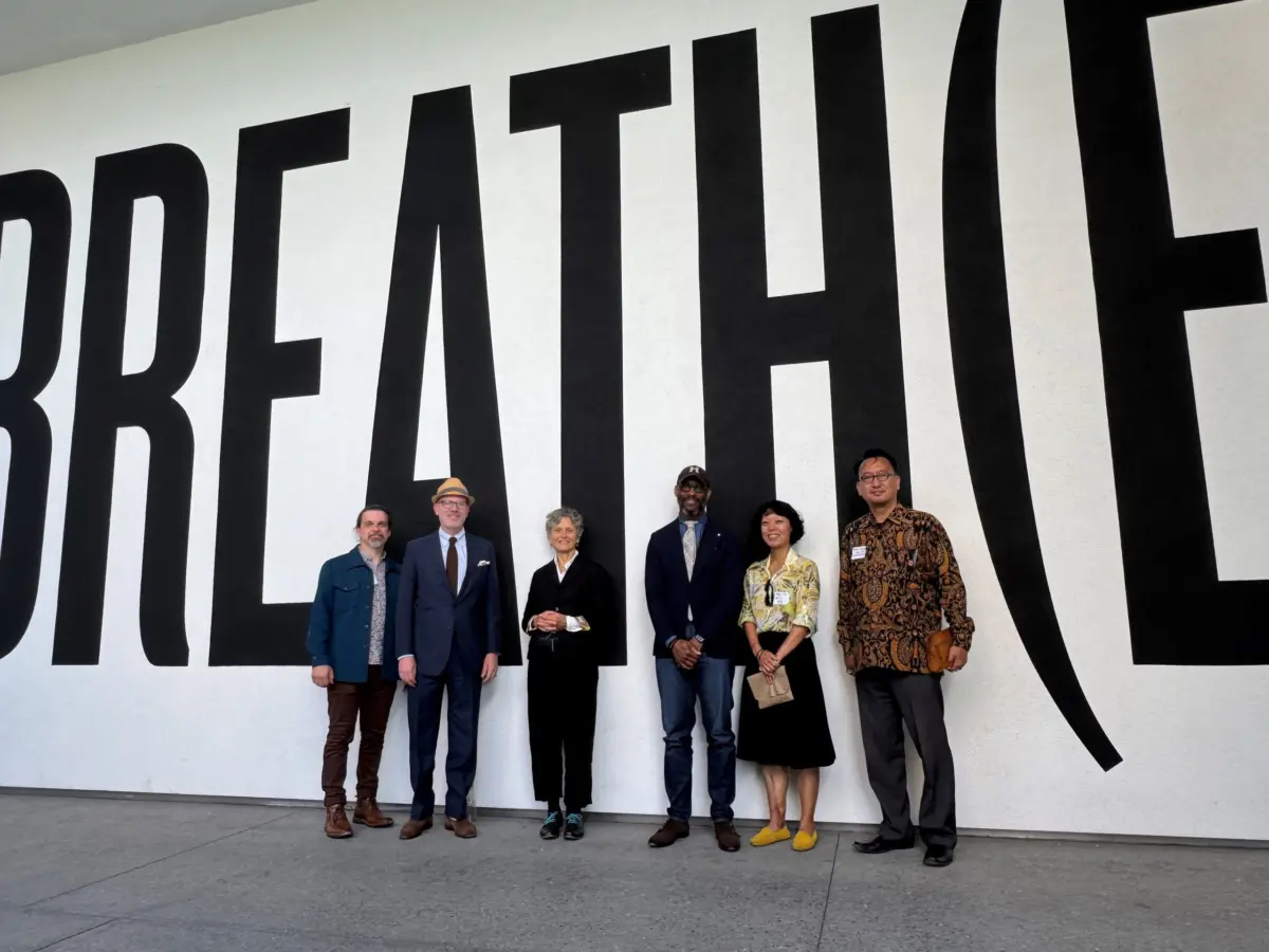 Six workshop participants stand together in front of a large wall mural spelling out "BREATH(E)" in oversized black letters.