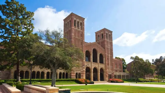 UCLA's Royce Hall with its twin brick towers, seen across a lawn and fountain under a blue sky.
