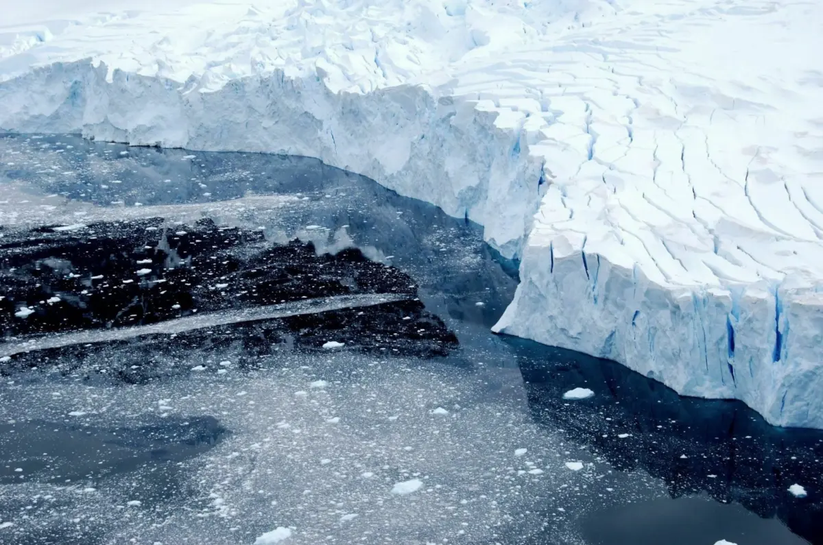 A towering ice shelf edge meets dark polar water scattered with broken ice fragments.