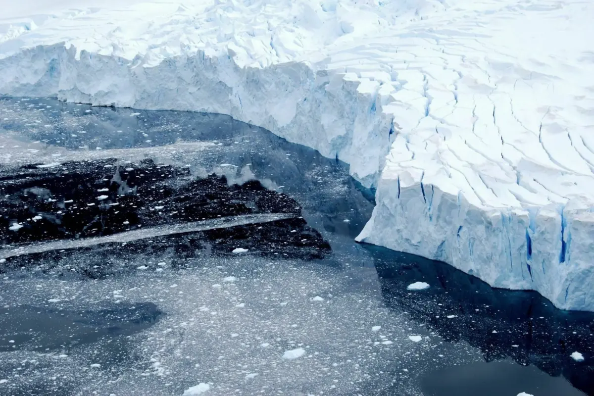 A towering ice shelf edge meets dark polar water scattered with broken ice fragments.
