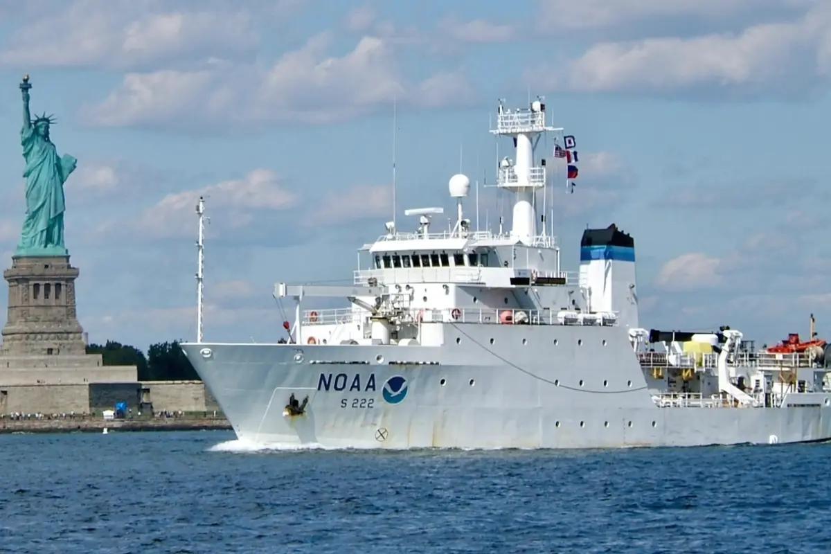 A NOAA hydrographic survey ship underway in New York Harbor, passing the Statue of Liberty.