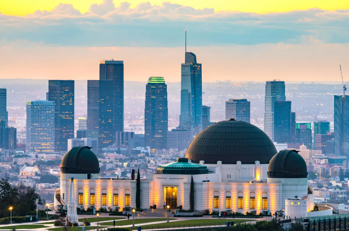 Griffith Observatory lit at dusk with the downtown Los Angeles skyline rising behind it.