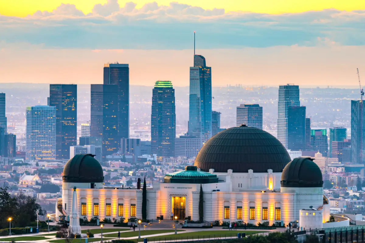 Griffith Observatory lit at dusk with the downtown Los Angeles skyline rising behind it.