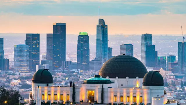 Griffith Observatory lit at dusk with the downtown Los Angeles skyline rising behind it.