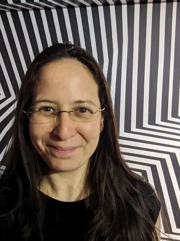 Jasmine Brackett - A woman with long dark hair and glasses in front of a striped geometric background