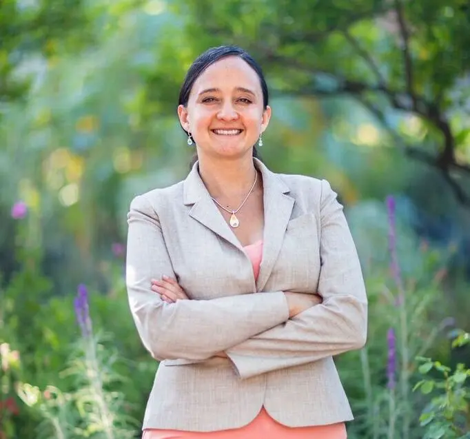 Portrait of a faculty member standing outdoors in a garden with flowering plants and trees.
