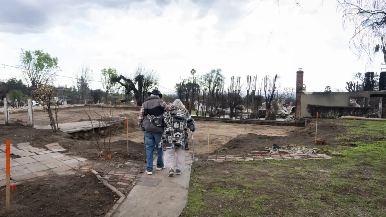 Image of two people walking towards the remnants of their home, which was burned in the winter 2025 wildfires.