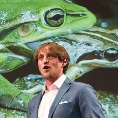 Anthony Waddle speaking on stage in front of a large projected image of frogs
