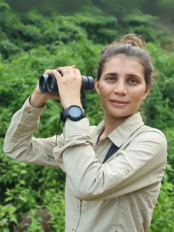 Seema Lokhandwala holding binoculars at a green field site