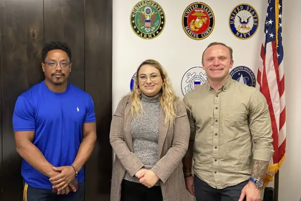 Jason Williams (left), Jade Knighton, and Tyrus Korecki. Members of the Vet in STEM group, standing next to the US flag, in front of a wall with US military insignia displayed.