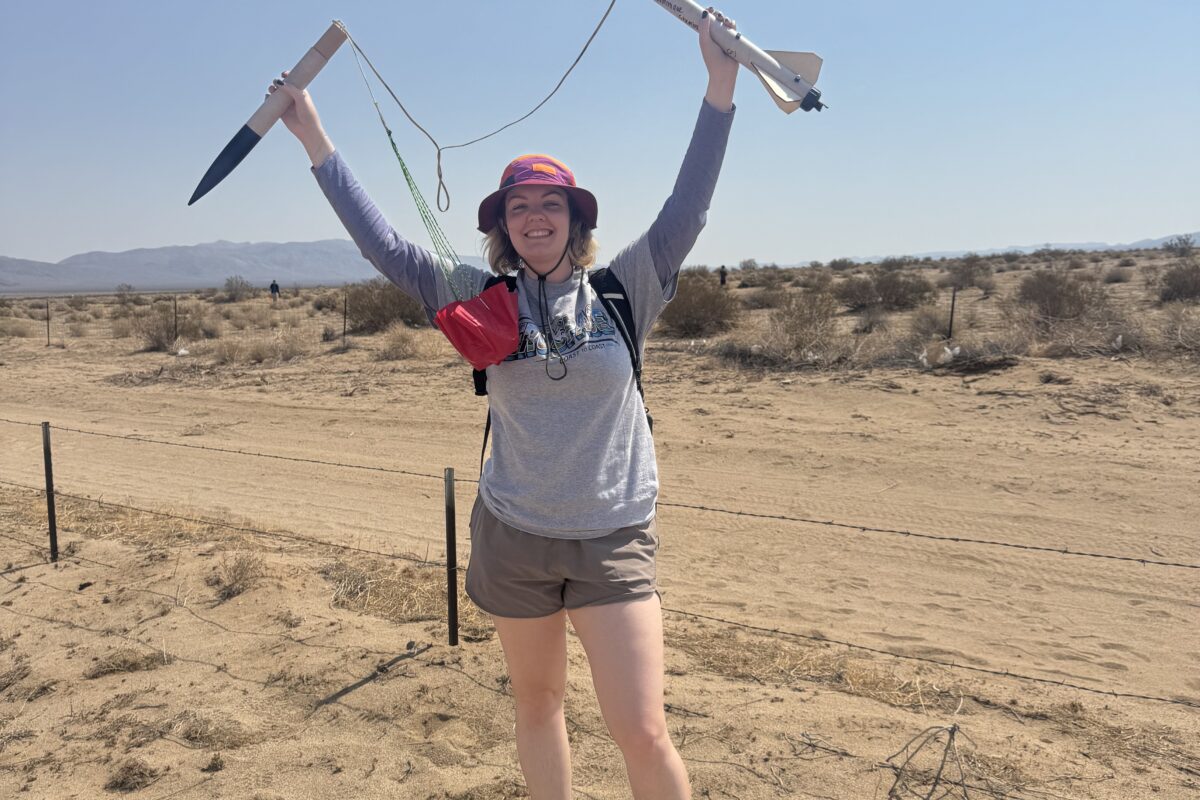 Nique holds a launched rocket up over her head in the desert.