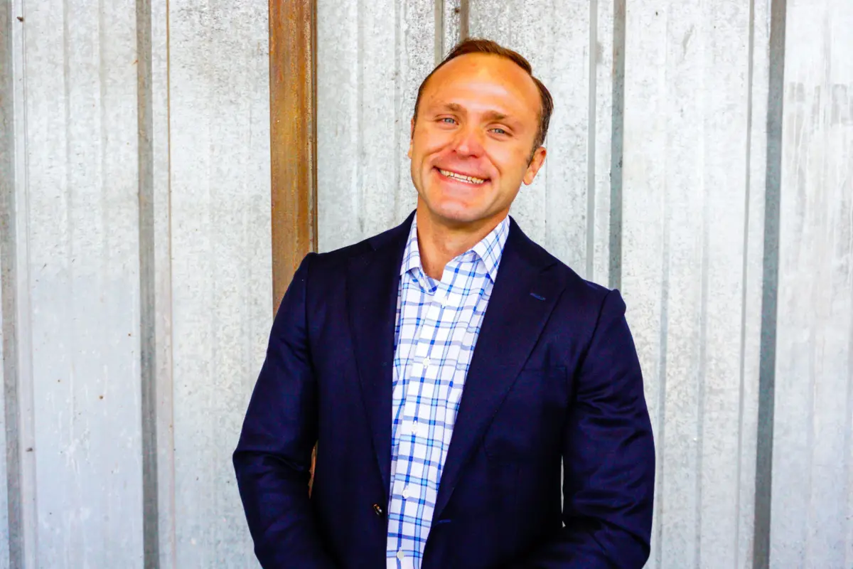 Tyrus Korecki, a smiling man in a smart blue and white checked shirt and dark blue blazer.