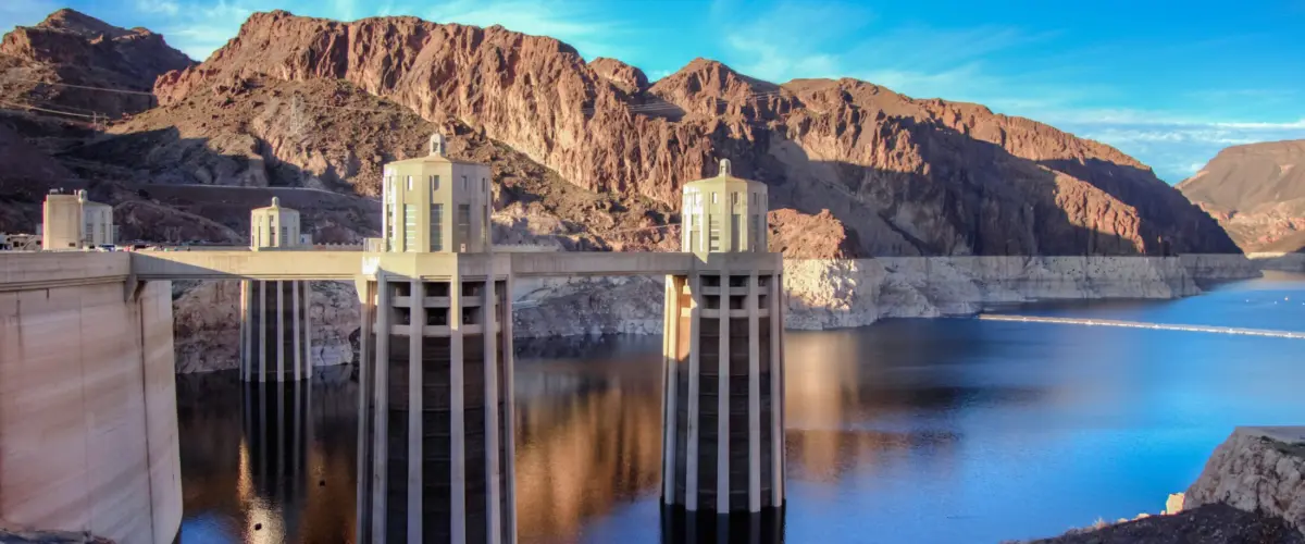 A view of Hoover Dam’s intake towers rising above the low water level of Lake Mead, with a visible bathtub ring along the surrounding canyon walls.