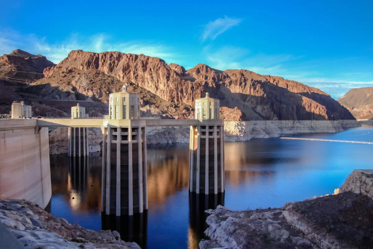 A view of Hoover Dam’s intake towers rising above the low water level of Lake Mead, with a visible bathtub ring along the surrounding canyon walls.