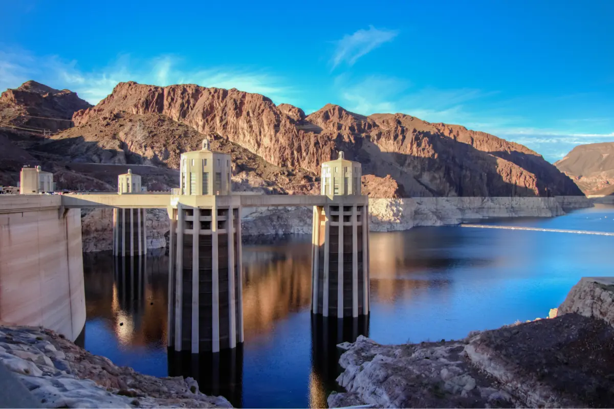 A view of Hoover Dam’s intake towers rising above the low water level of Lake Mead, with a visible bathtub ring along the surrounding canyon walls.