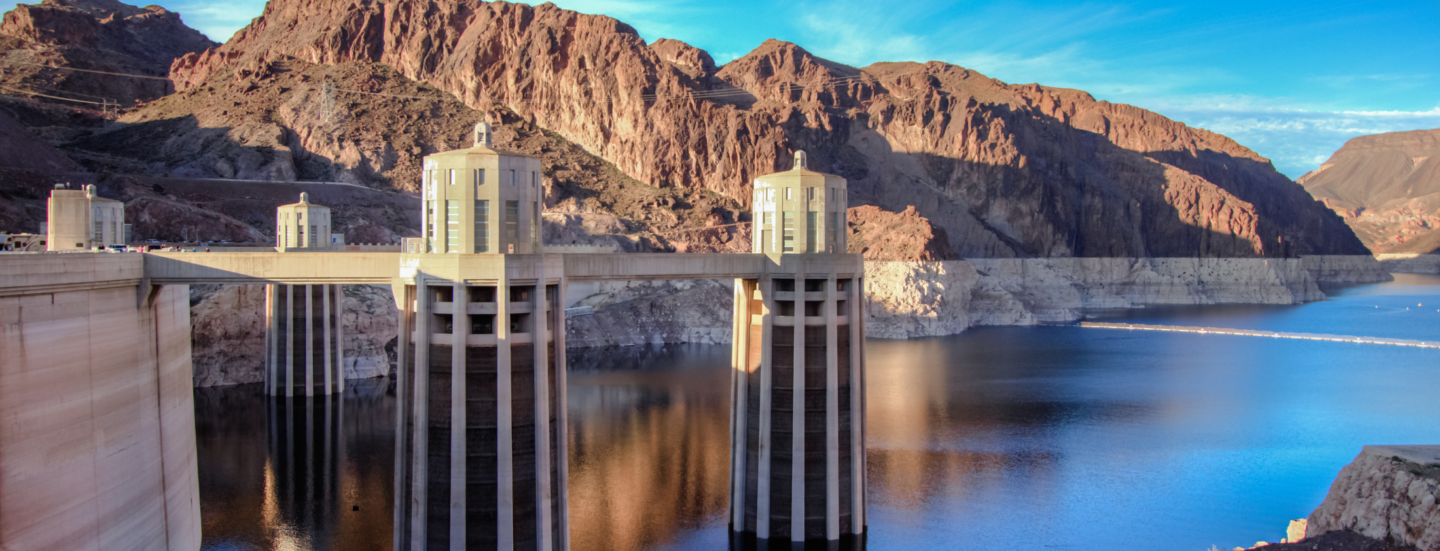A view of Hoover Dam’s intake towers rising above the low water level of Lake Mead, with a visible bathtub ring along the surrounding canyon walls.