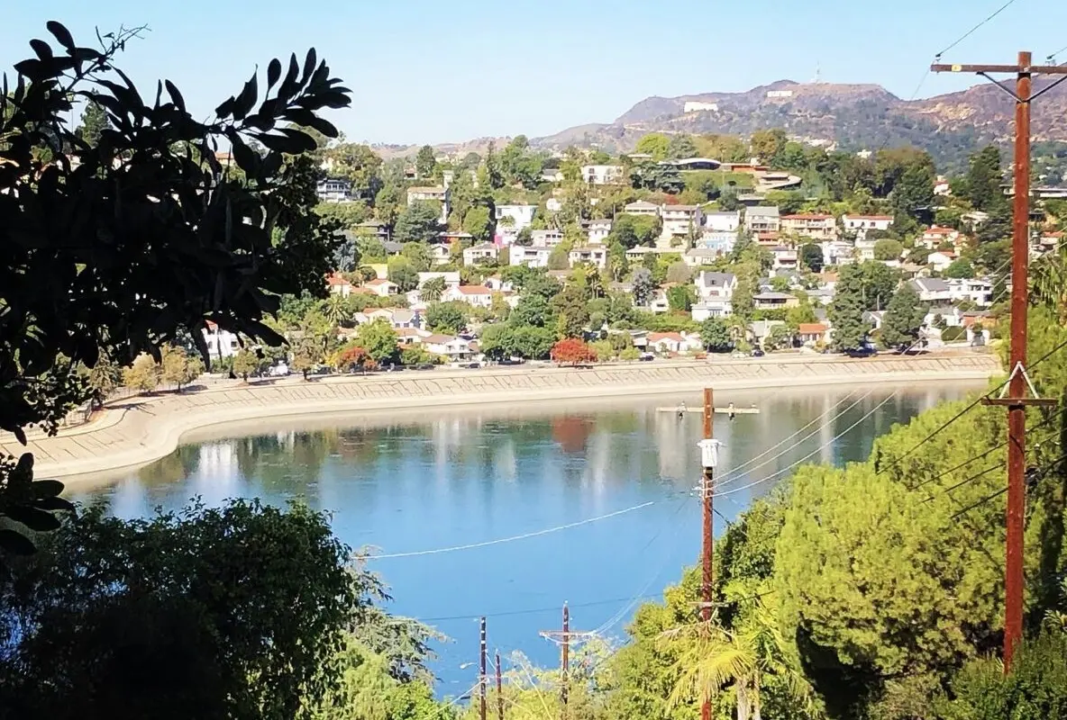 Silver Lake Reservoir ringed by hillside homes, with Griffith Observatory and the Hollywood Sign in the distance.