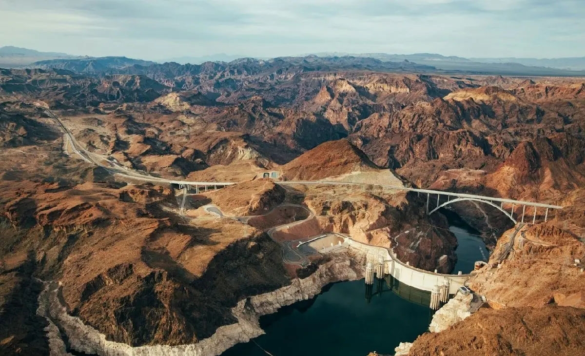 Aerial view of Hoover Dam and its bypass bridge set in the rugged red rock canyons of the Colorado River.