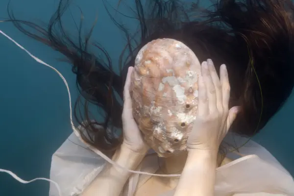 Woman underwater with shell covering her face