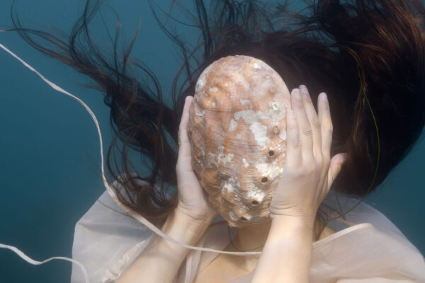 Woman underwater with shell covering her face