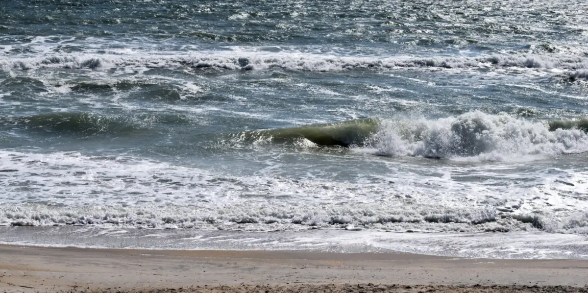 Choppy surf breaking in whitewater lines onto an empty sandy beach.