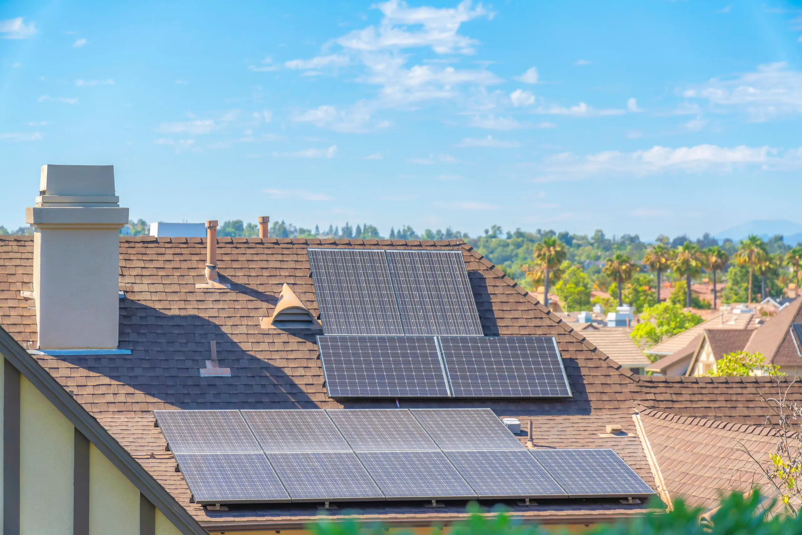 Solar panels on top of the asphalt composite shingles roof of a house at Ladera Ranch, California. Roof of a house in a residential community with palm trees outdoors against the sky.